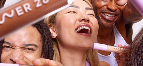 Several people of different races and skin tones holding a Tower 20 lip stick, all smiling as if at a party